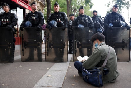 A demonstrator sits reading a book in front of gendarmerie officers holding riot shields