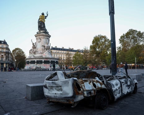 A burnt-out car near the Marianne statue at the Place de la Republique, with a yellow vest put on it