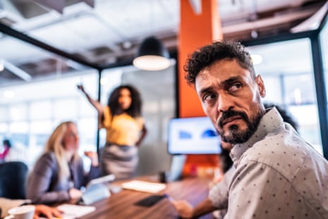 A man of colour with short brown hair looking angry in an office