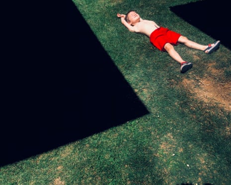 A young shirtless boy in red shorts lies on grass with arms stretched above his head