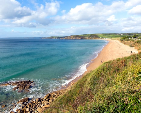 Praa Sands beach in Cornwall curves along a blue bay with grassy cliffs